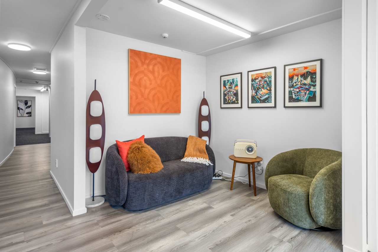 The entry lounge, with a dark sofa, green armchairs and an orange artwork